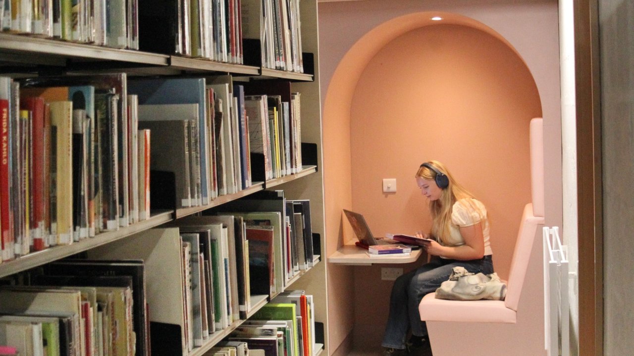 student wearing headphones sitting in a solo study booth