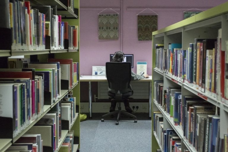 Falmouth Library Person Studying on Computer with Shelves in Foreground