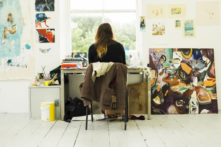 Student sitting in front of a window surrounded by artwork