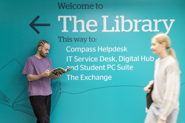 two students standing in front of the library welcome sign